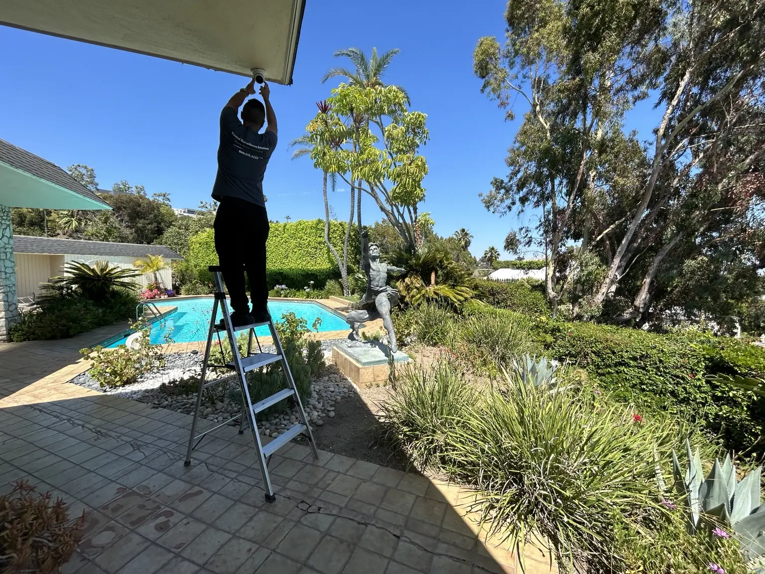 Three Factor Security technician fully visible while installing an exterior camera beside a residential pool — Three Factor Security fieldwork in Beverly Hills